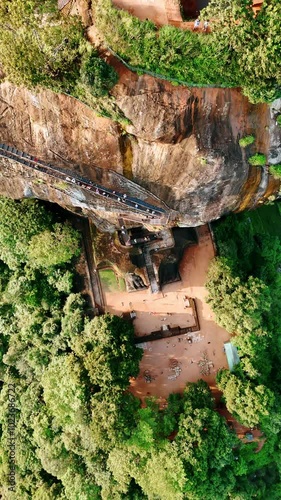 Tourists go up by the stairs of the stunning mountain. Drone footage above the Sigiriya Fortress in Sri Lanka. Vertical video.