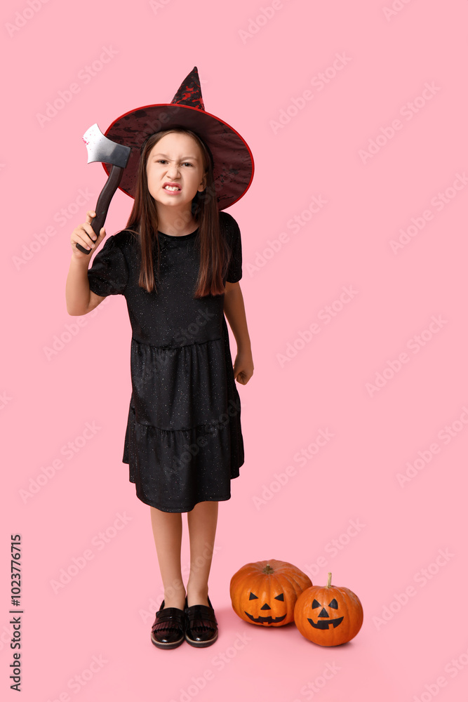 Cute little girl dressed for Halloween as witch with axe and pumpkins on pink background