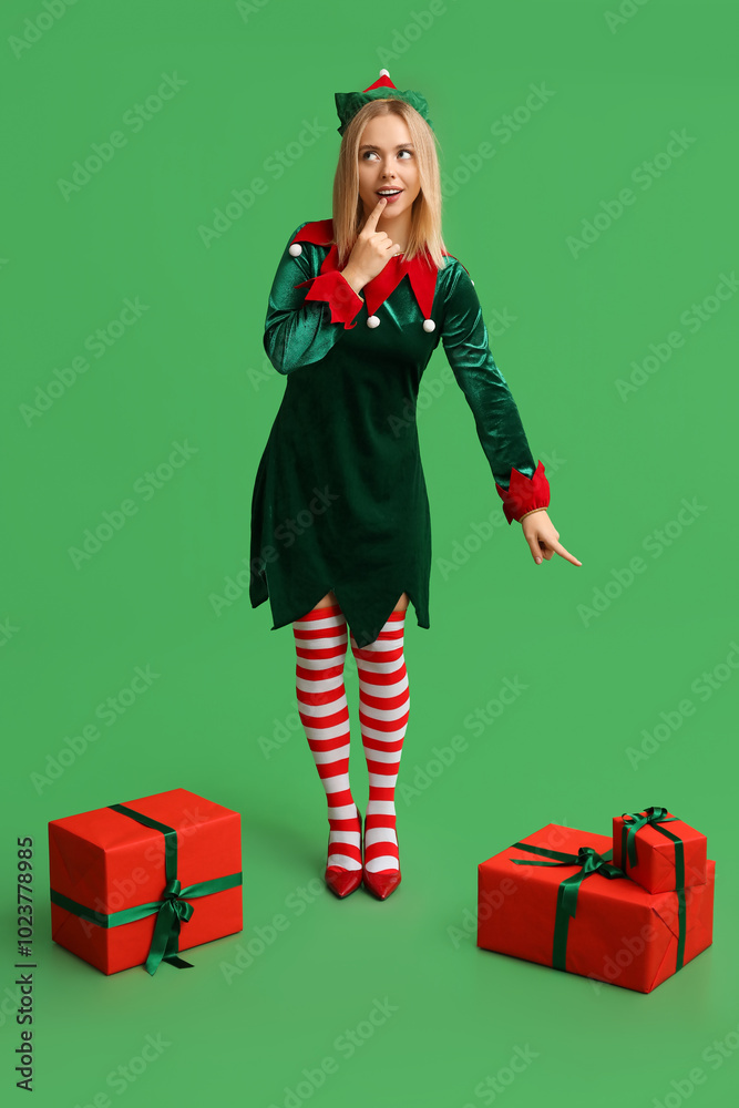 Beautiful young woman in elf costume with Christmas gift boxes on green background
