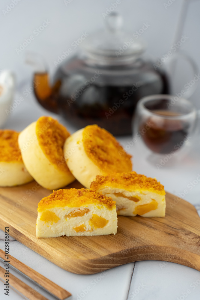 Delicious slices of peach cheesecake with kramble filling on a wooden board and hot tea in a cozy atmosphere. Concept of home baking, comfort desserts and relaxing tea drinking. Delicious slices of peach cheesecake with kramble filling on a wooden board and hot tea in a cozy atmosphere. Concept of home baking, comfort desserts and relaxing tea drinking.