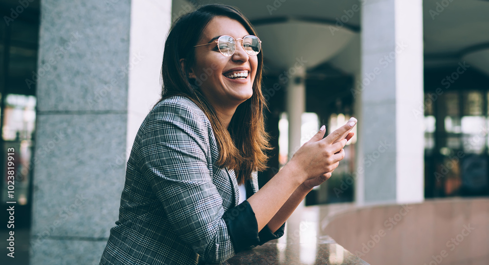 © BullRun - Portrait of cheerful hipster girl with modern cellular phone in hands laughing during leisure time on urban setting, happy Turkish millennial woman smiling from received content text on cellphone © BullRun - Portrait of cheerful hipster girl with modern cellular phone in hands laughing during leisure time on urban setting, happy Turkish millennial woman smiling from received content text on cellphone