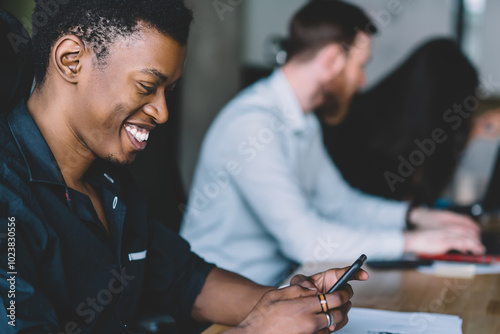 Cheerful african business man having break from working process with colleagues in office and enjoying chatting with friends via mobile application using free wifi connection from company office