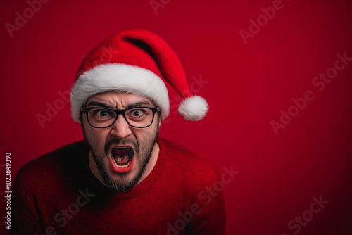 Angry man in Santa hat screaming in frustration on red background. Humorous Christmas portrait perfect for funny holiday cards or advertising with seasonal humor.