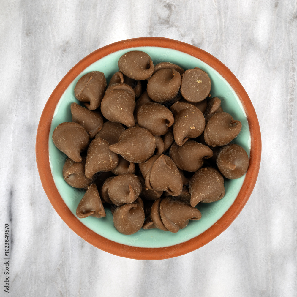 Fototapeta premium Bowl filled with milk chocolate chips on a gray marble background.