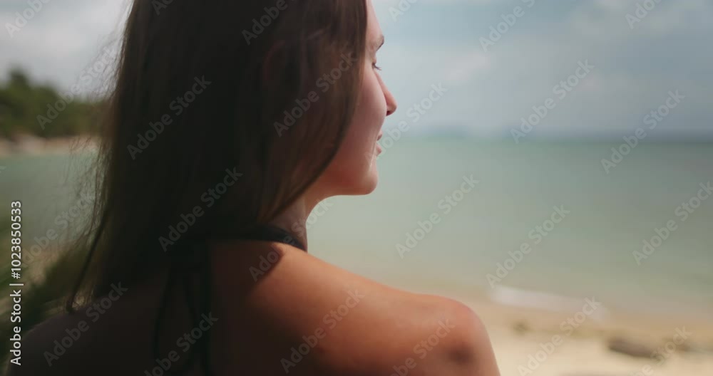 Young woman is enjoying the view of the ocean on a sunny day in thailand. The wind is blowing through her hair as she takes in the beauty of her surroundings Young woman is enjoying the view of the ocean on a sunny day in thailand. The wind is blowing through her hair as she takes in the beauty of her surroundings