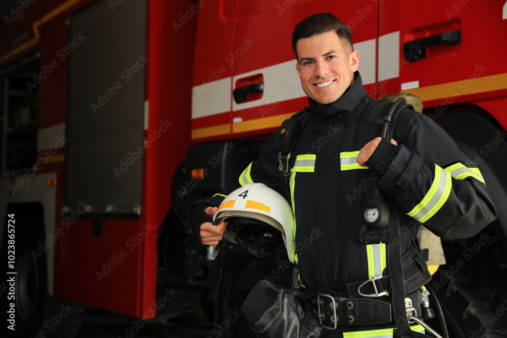 Portrait of firefighter in uniform with helmet near fire truck at station, space for text