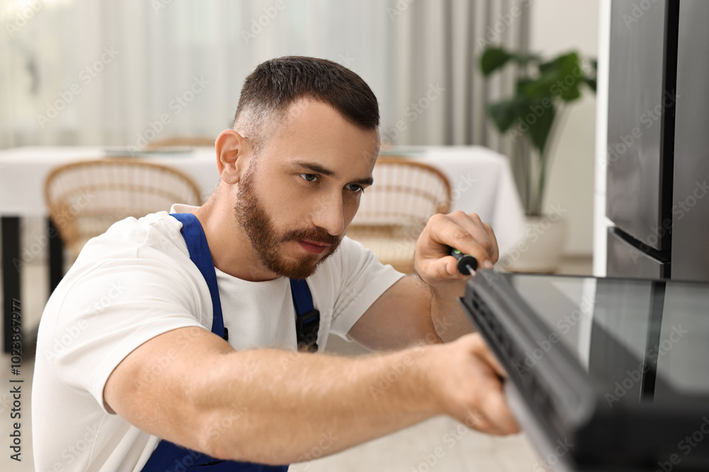 Repairman with screwdriver fixing oven at home