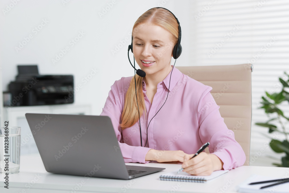 Interpreter in headset taking notes while having video chat via laptop at table indoors Interpreter in headset taking notes while having video chat via laptop at table indoors
