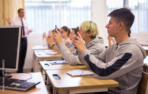 Teen students using smartphones to find necessary information on lecture in college class photo