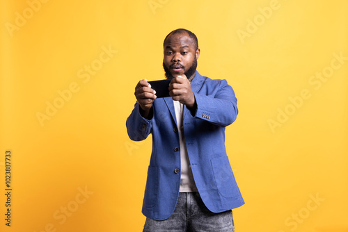 BIPOC man playing intense singleplayer videogames on smartphone, enjoying hobby. African american gamer enjoying entertaining interactive game on phone, having fun, studio background photo