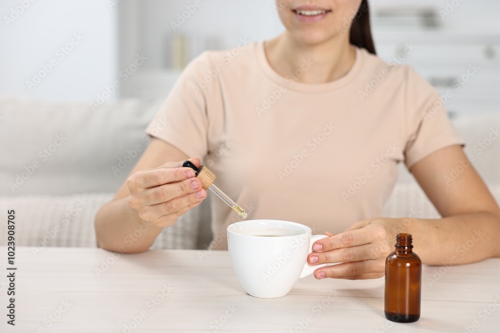 Young woman putting CBD tincture into cup with drink at white wooden table, closeup Young woman putting CBD tincture into cup with drink at white wooden table, closeup