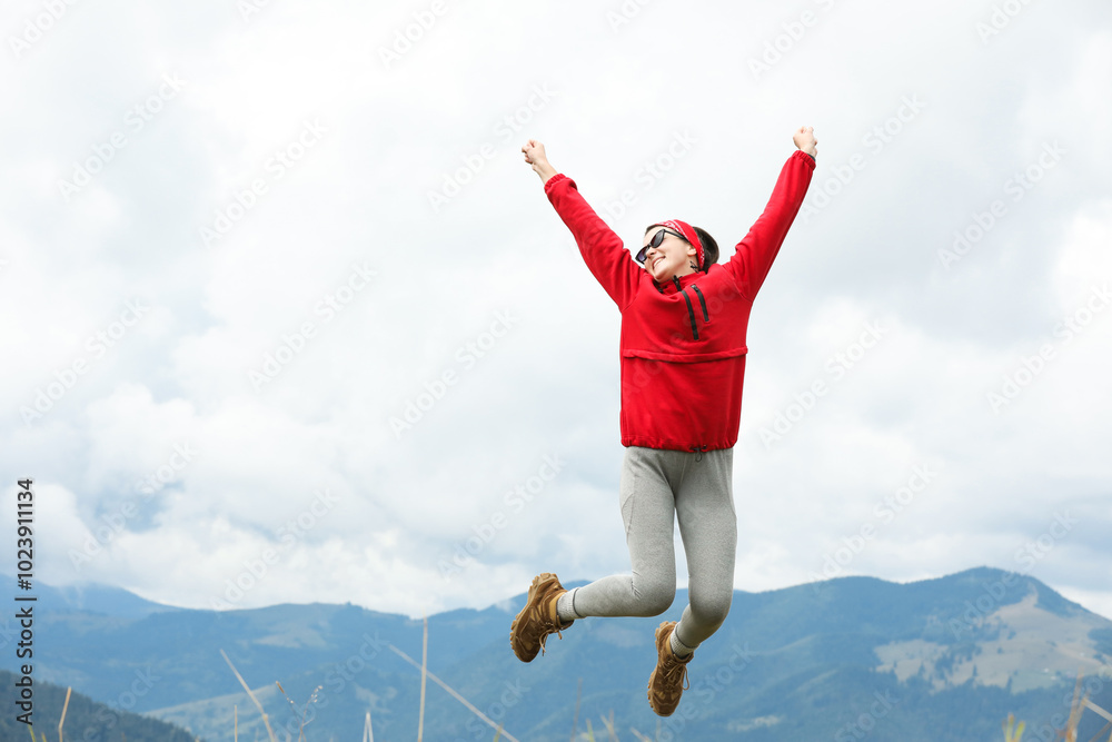 Happy young hiker jumping in mountains, low angle view. Space for text Happy young hiker jumping in mountains, low angle view. Space for text