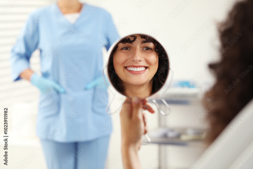 Patient looking in mirror and doctor in clinic, selective focus. Dental veneers Patient looking in mirror and doctor in clinic, selective focus. Dental veneers