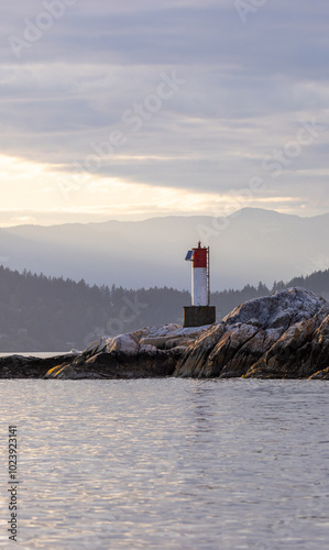 Scenic View of Lighthouse on Rocky Shore at Sunset in Vancouver, BC, Canada With Mountain Range in the Background photo