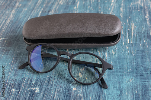 Sleek and modern black-rimmed glasses and gray glasses case on a blue table.