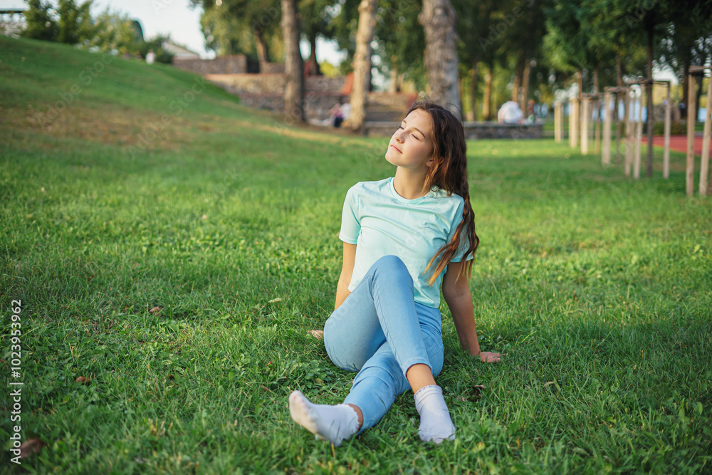 Fototapeta premium Portrait of cute charming lady sitting lend ground fresh green grass enjoy sun nature harmony student resting from city crowd people wear t-shirt jeans colorful park outdoors
