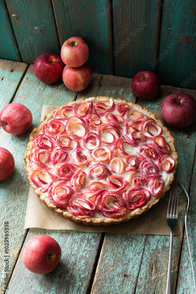 Apple pie with apples in the shape of roses on wax paper with red apples behind and two thin metal forks Apple pie with apples in the shape of roses on wax paper with red apples behind and two thin metal forks