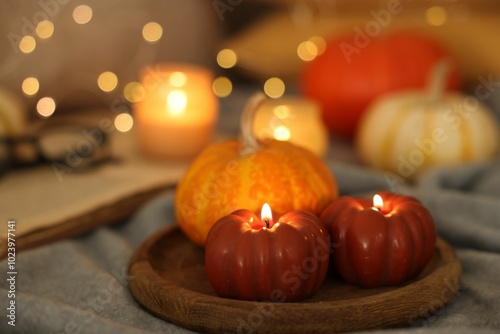 Burning candles and pumpkin on grey cloth against blurred lights, closeup. Autumn atmosphere