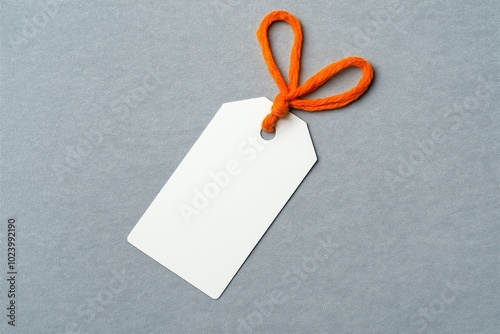 A blank white tag tied with an orange string against a light gray background, ideal for marketing and branding concepts, showcasing simplicity and versatility.