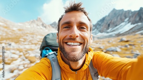 A happy hiker in a yellow jacket with a large backpack beams at the camera, surrounded by snow-capped mountains and clear skies, exuding positivity.