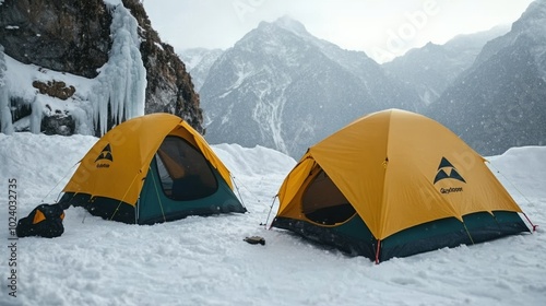 Two yellow tents set in snowy mountains under a cloudy sky.