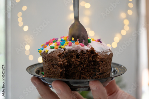 mano sosteniendo plato de pastel de chocolate mordido con fondo de luces desenfocadas  photo