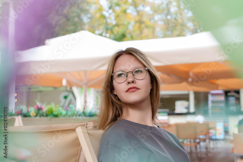 In the relaxed ambiance of an outdoor cafe, a teenage customer appears transfixed, her gaze directed inwardly as she ponders something beyond the physical world. photo