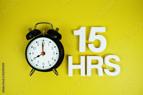 15 Hrs alphabet letters and alarm clock top view on yellow background