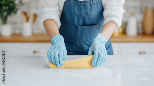 A person wearing blue gloves is cleaning kitchen countertop with yellow sponge, showcasing tidy and organized space. focus is on cleanliness and care in home maintenance