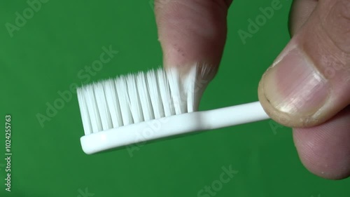 Close up shot male hand index finger touching to check softness of toothbrush bristles with green screen fabric in background.