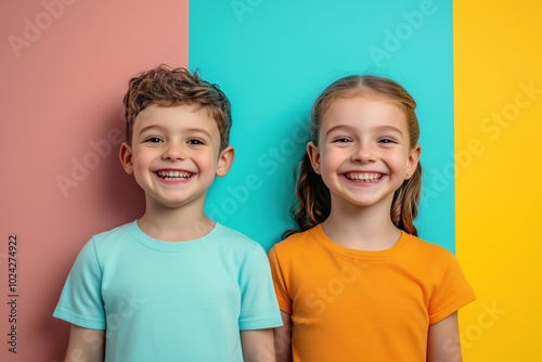 Two cheerful children with bright smiles standing against a colorful wall in a playful setting