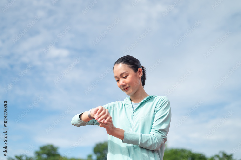 Young Asian woman wearing blue sportswear Stand and hold the watch to measure your heart rate while exercising. outdoor exercise Exercise in the stadium Heartbeat, pulse measurement, active living Young Asian woman wearing blue sportswear Stand and hold the watch to measure your heart rate while exercising. outdoor exercise Exercise in the stadium Heartbeat, pulse measurement, active living