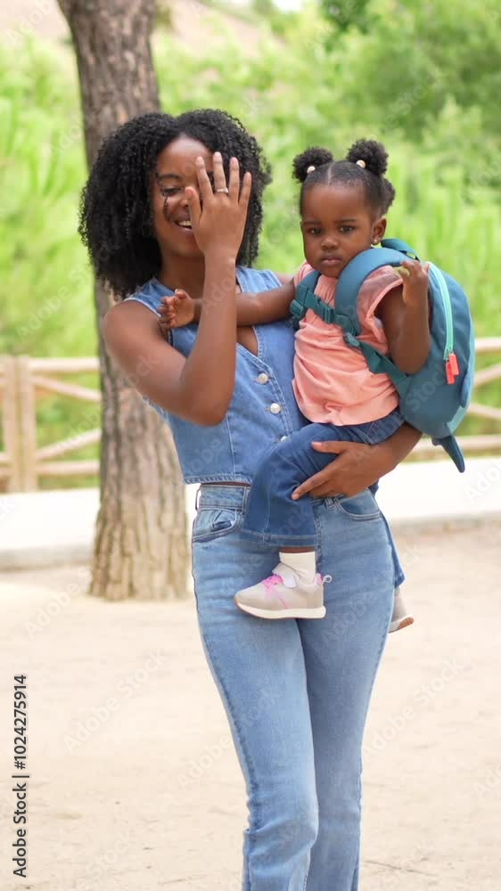 African woman with a girl in her arms arrives at the park where their grandmother is waiting for them African woman with a girl in her arms arrives at the park where their grandmother is waiting for them