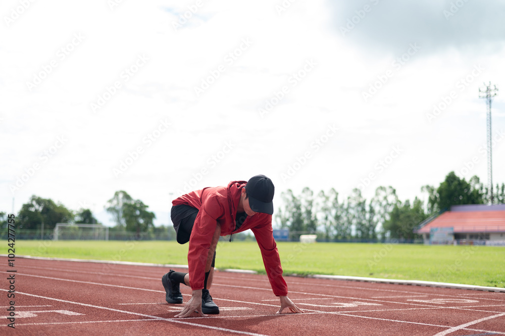 Cool Asian guy wearing red exercise clothes. Starting out on the running lane in the stadium. Both hands are placed on the floor close to the body. outdoor exercise maintaining health active living Cool Asian guy wearing red exercise clothes. Starting out on the running lane in the stadium. Both hands are placed on the floor close to the body. outdoor exercise maintaining health active living