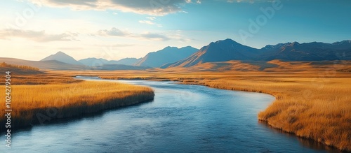 Winding river through a golden field with mountains in the distance at sunset.