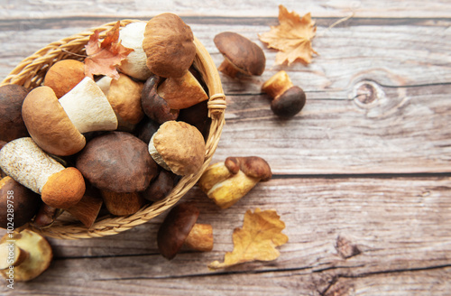 A woven basket filled with various mushrooms and autumn leaves on a wooden surface in a cozy kitchen setting