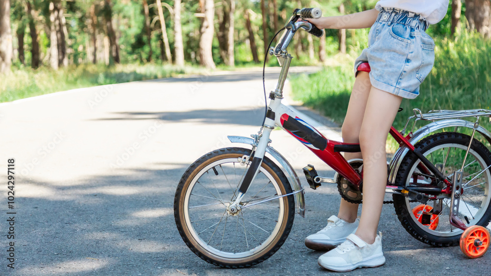 Fototapeta premium Child riding a bike in summer park. Children learning to drive a bicycle on a driveway outside. Kid riding bike. Child on bicycle, bike outdoor close up