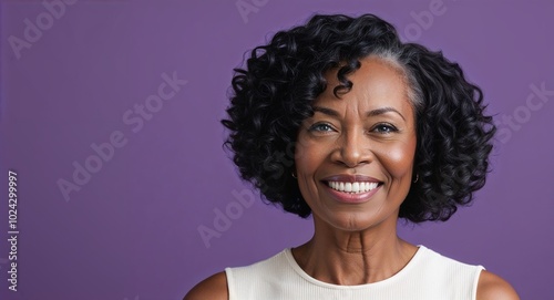 Middle aged Black woman with soft features and short curly hair smiling light purple background