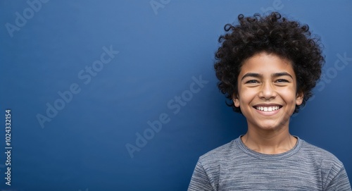 Teen mixed race boy with strong jawline and curly hair smirking dark blue background