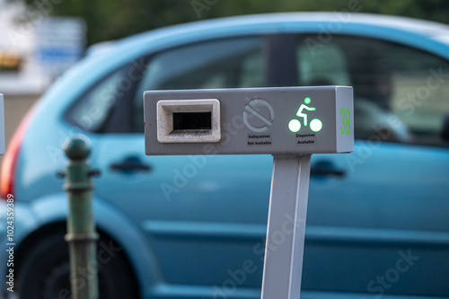A bike-sharing station displays available bikes while a car is parked nearby.