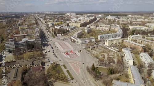 Aerial view of traffic in the city on a street with a roundabout and a square. Low-rise buildings