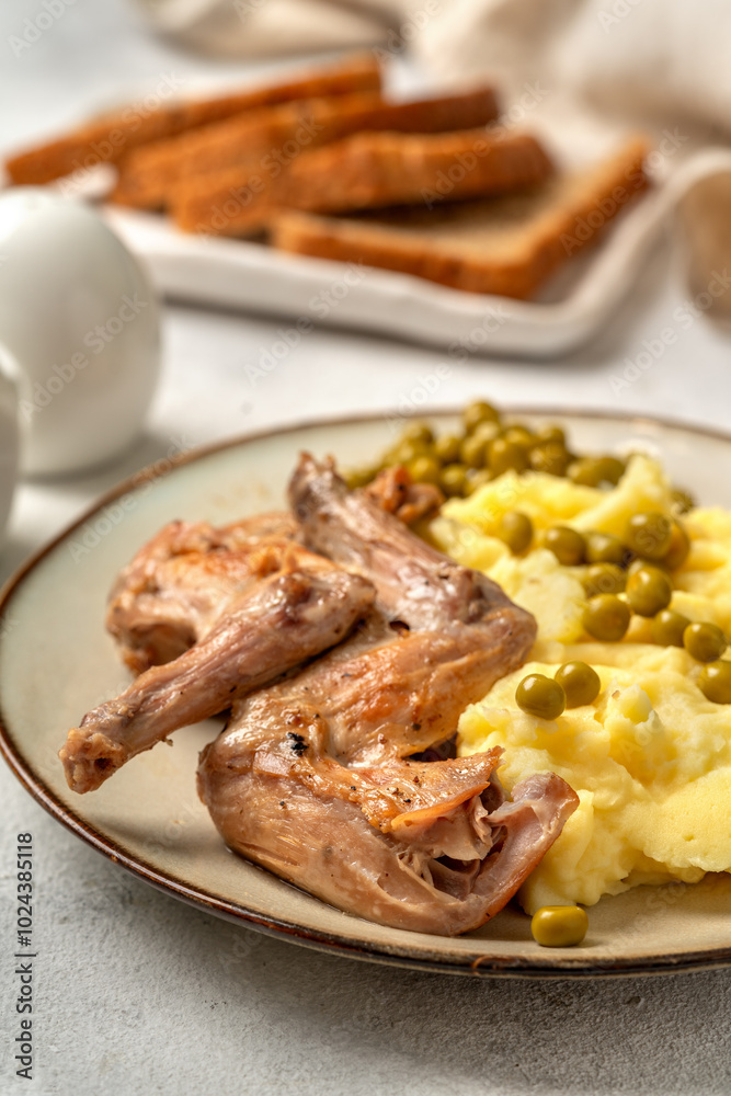 Pieces of rabbit stew, mashed potatoes and green peas on a plate on a bright table closeup