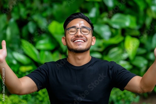 Man with glasses is smiling and holding his hands up in the air. Concept of joy and positivity. happy man in nature with lot of greenery around him siling