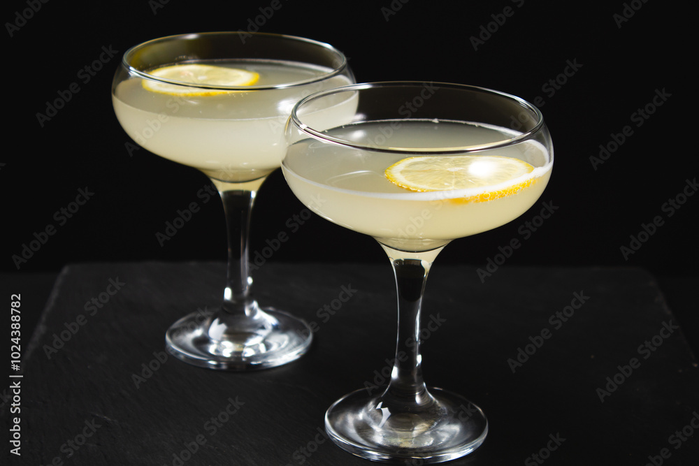 Yellow cocktail with lemon wedge on black background Yellow cocktail with lemon wedge on black background