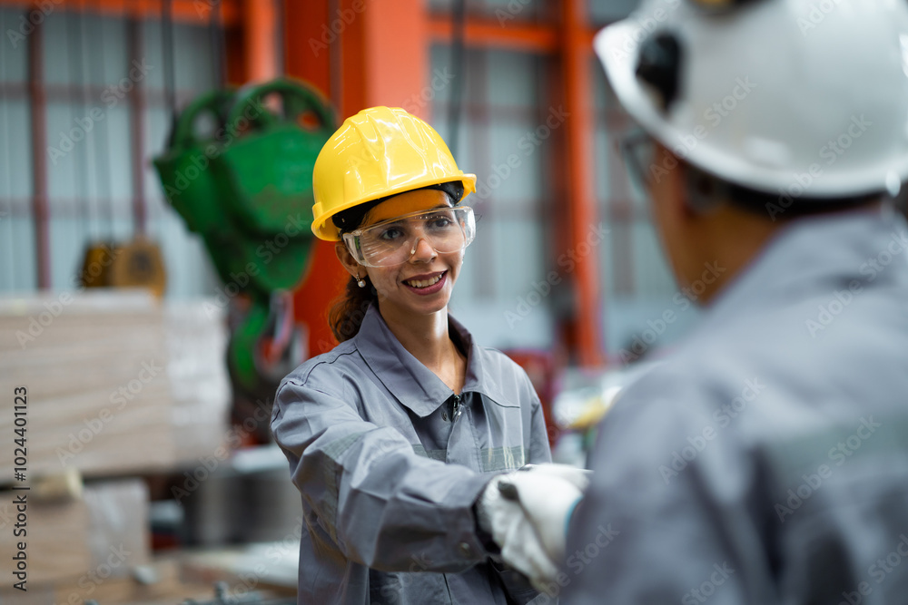 Two people in a factory, one wearing a yellow helmet and the other wearing a grey jacket. They are shaking hands Two people in a factory, one wearing a yellow helmet and the other wearing a grey jacket. They are shaking hands