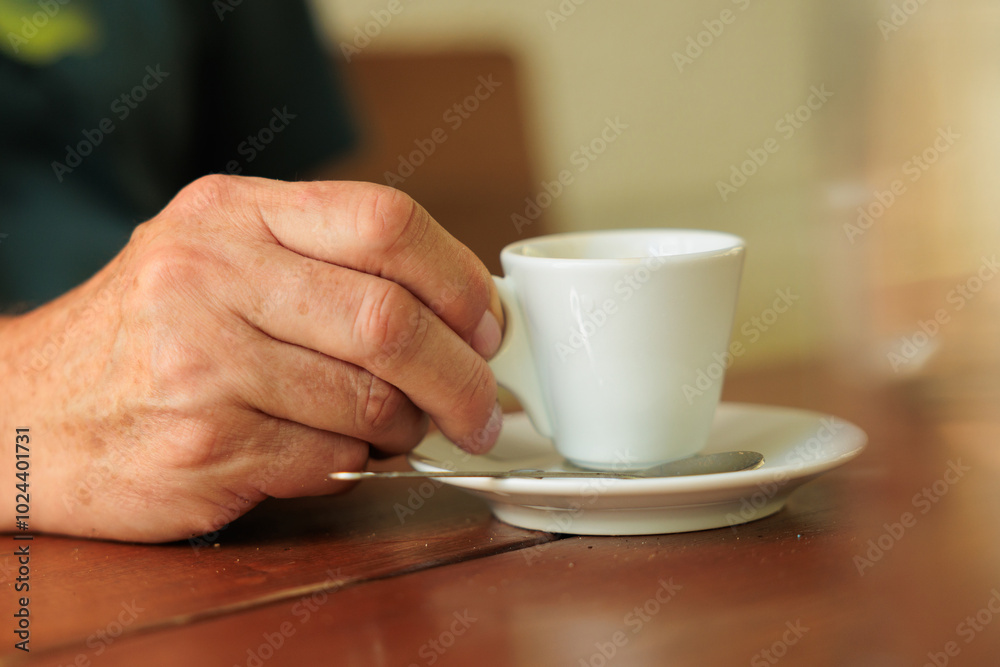 Dettagli in primo piano della mano di un uomo adulto irriconoscibile mentre tiene una tazzina da caffè bianca