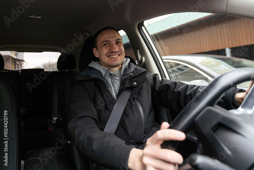 Success in motion. Handsome young man in full suit smiling while driving a car