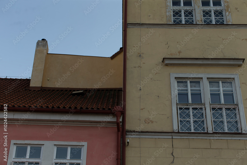 There is a yellow building located right next to a pink building, and this pink structure features several white windows on its facade