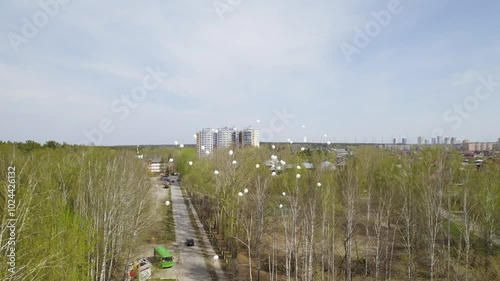 Aerial view of a lot of white balloons going up and flying over the city. A city with high-rise buildings and private one-story houses