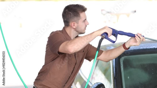 Young man cleaning car using high pressure water on self-service car wash. 